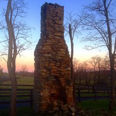 an old brick fireplace in the middle of a field with trees and fence around it