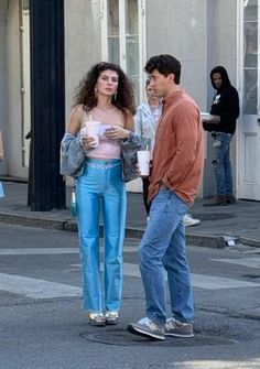 a man and woman standing on the street talking to each other while holding coffee cups