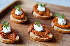 small pieces of bread topped with meat and sour cream on a wooden tray, ready to be eaten