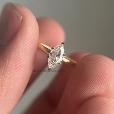 a close up of a person's hand holding a ring with a diamond on it