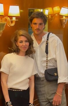 a man and woman standing next to each other in front of a wall with lamps