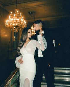 a man and woman standing next to each other in front of a chandelier