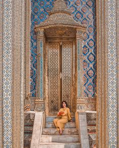 a woman sitting on some steps in front of a wall with intricate designs and patterns