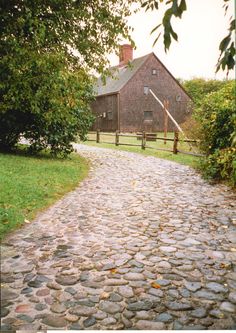 a cobblestone path leading to a brick building in the distance with trees on either side