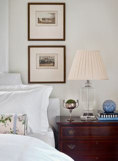 two framed pictures on the wall above a bed with white linens and blue accents