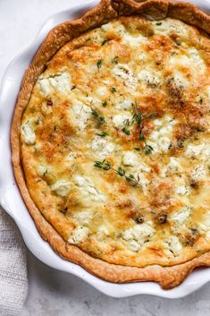 a quiche with cheese and herbs in a white dish on top of a table