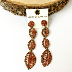 Pictured are dangly circle beaded post back football earrings in brown. They are propped up against a circular piece of wood on a white background. Football Beaded Earrings, Kansas City Chiefs Earrings, Georgia Bulldog Earrings, Tennessee Vols Earrings, Football Earrings, Giddy Up Glamour, Sale Items, Graphic Tees, Football