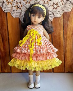 a doll is wearing a dress made out of ruffles and yellow ribbon, while standing in front of a lace doily