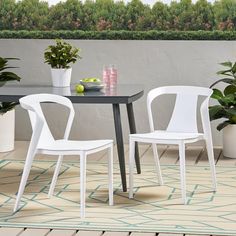 two white chairs sitting at a black table on top of a rug next to potted plants