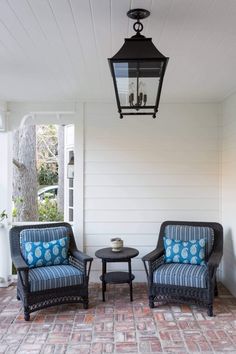 two chairs and a table sitting on a brick patio next to a light fixture hanging from the ceiling