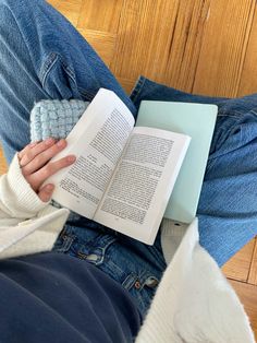 a person is sitting on the floor reading a book and holding a knitted mitt