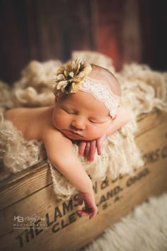 a baby laying on top of a wooden crate wearing a white lace headband and flower in her hair