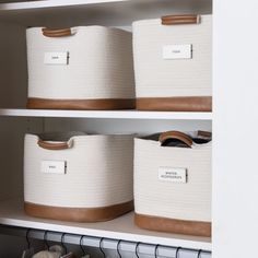 three white baskets with leather handles and labels on them are sitting on shelves in a closet