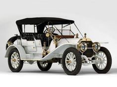 an antique white car with gold trim on the front and back wheels, parked against a white background