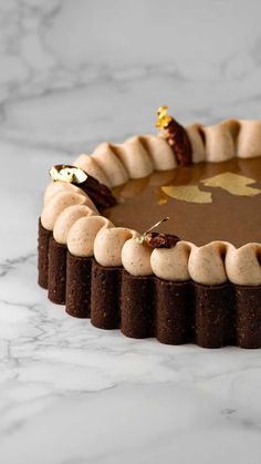 a chocolate cake with white frosting and gold decorations on it's edges, sitting on a marble surface