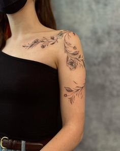 a woman with a flower tattoo on her left arm and shoulder, standing in front of a gray wall