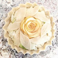 an apple pie with leaves and a spiral design on top is sitting on a marble countertop