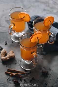 two glasses filled with orange juice and cinnamon sticks