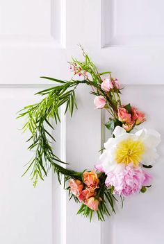 a floral wreath hangs on the front door with greenery and pink, yellow and white flowers