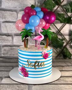 a blue and white cake with pink flamingos, palm trees, and balloons on top