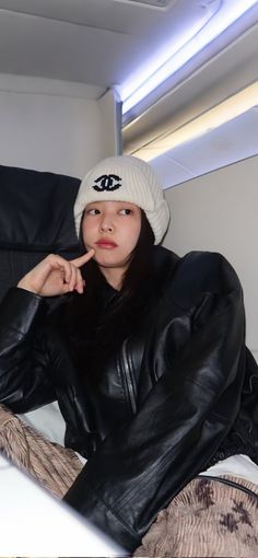 a woman wearing a black leather jacket and white hat sitting on top of a couch