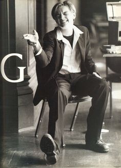 a black and white photo of a man in a suit sitting on a chair smiling