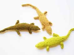 three crocheted lizards sitting next to each other on a white surface, one is yellow and the other is green