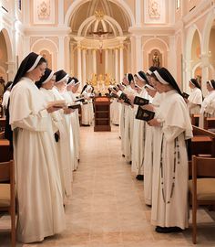 a group of women in white robes standing at the end of a church aisle holding books