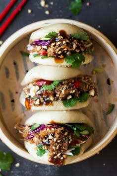 three buns filled with meat and vegetables in a wooden bowl next to chopsticks