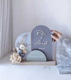 a person holding up a sign with flowers on it next to a white wall and window