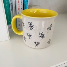 a yellow and white coffee mug sitting on top of a desk next to bookshelves