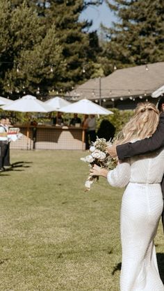 a bride and groom walking through the grass at their outdoor wedding ceremony with umbrellas in the background