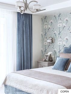 a bedroom with floral wallpaper and blue drapes on the window sill, along with a large bed