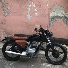 a black and brown motorcycle parked next to a pink wall with peeling paint on it