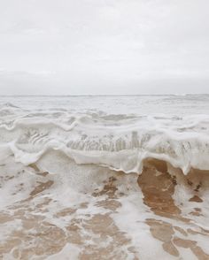 an ocean wave with white foam on the shore and brown sand in the foreground