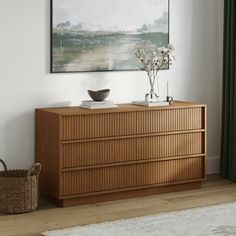 a wooden dresser sitting in front of a painting on the wall next to a basket