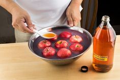 a person holding a spoon in a pan filled with apples and syrup next to a bottle of apple cider