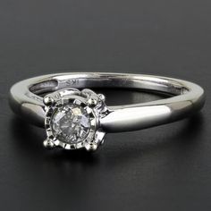 a white gold engagement ring with a diamond in the center, on a black surface