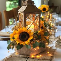 a lantern with sunflowers and greenery sits on a table set for dinner