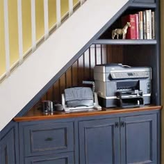 a bookshelf under the stairs with printer and printer on it