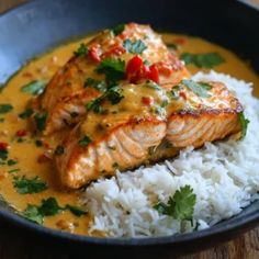 two salmon fillets on top of white rice in a black bowl with garnishes