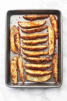 baked potato wedges in a baking pan on a marble countertop with seasoning