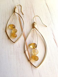 a pair of gold hoop earrings with citrine beads hanging from them on a white surface