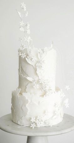 a white wedding cake with flowers on the top and bottom is sitting on a pedestal