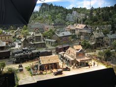 a model train set is shown in front of a mountain scene with buildings and cars