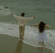 two people standing on the beach with their arms spread out and one person holding hands