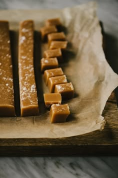 several pieces of caramel cheese sitting on top of a wooden cutting board with wax paper