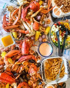 lobsters, corn and other seafood are on the table with different foods in bowls