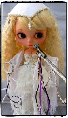 a doll with blonde hair wearing a white dress and holding a microphone in her hand