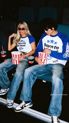 two people sitting next to each other with popcorn in their hands and sodas on their laps